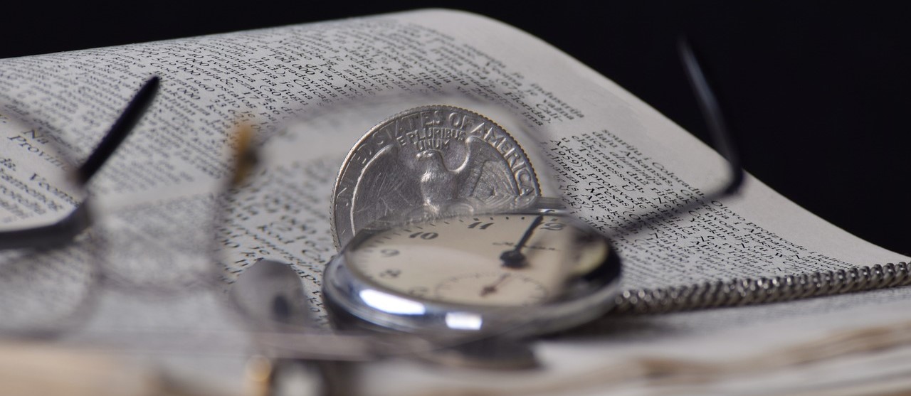 A coin, glasses and pocket watch on an opened book.
